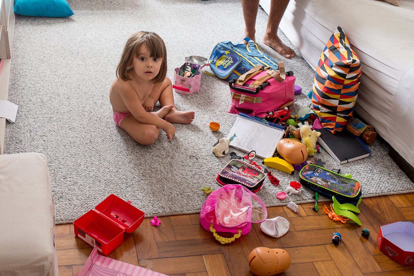 Criança sentada rodeada de brinquedos espalhados pelo chão, exemplo de fundo poluído